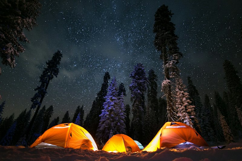 Trois tentes éclairées sous les étoiles en forêt